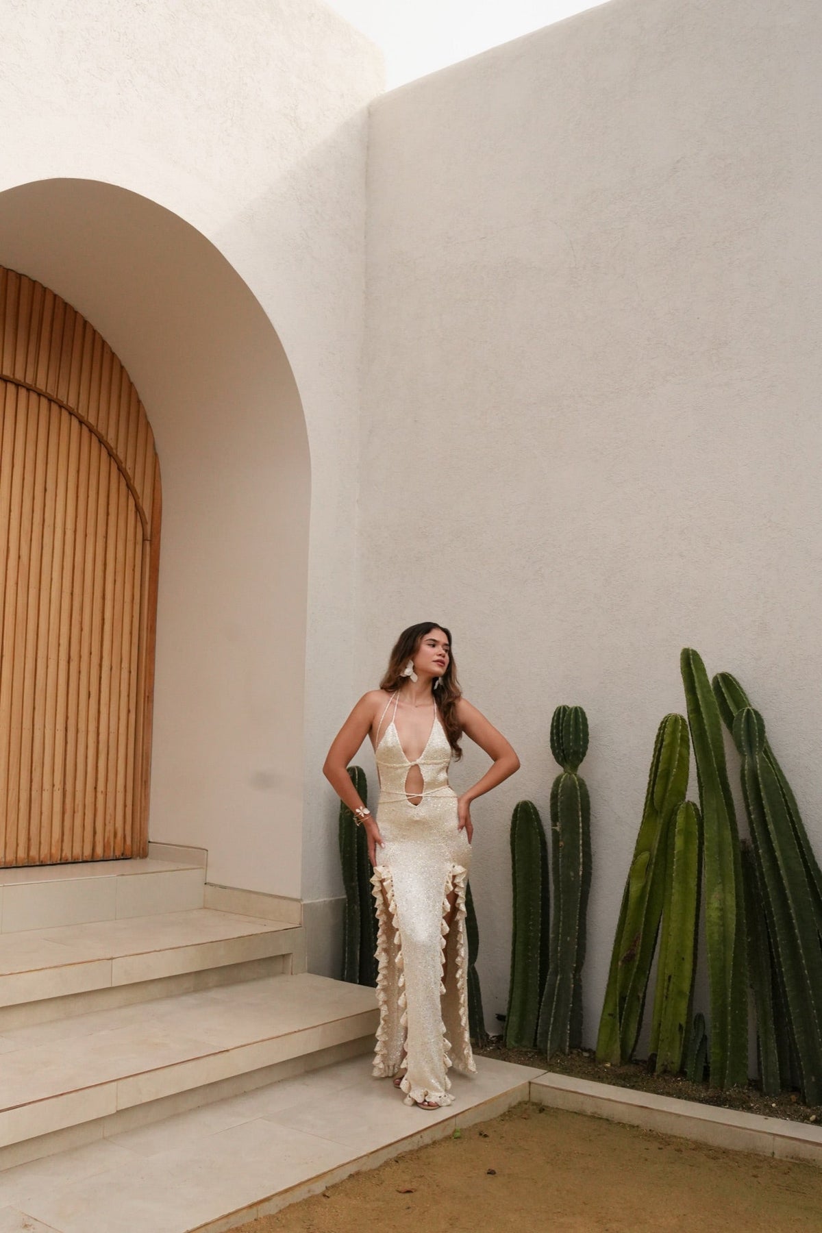 Clienta con vestido largo color marfil junto a un arco de madera y cactus